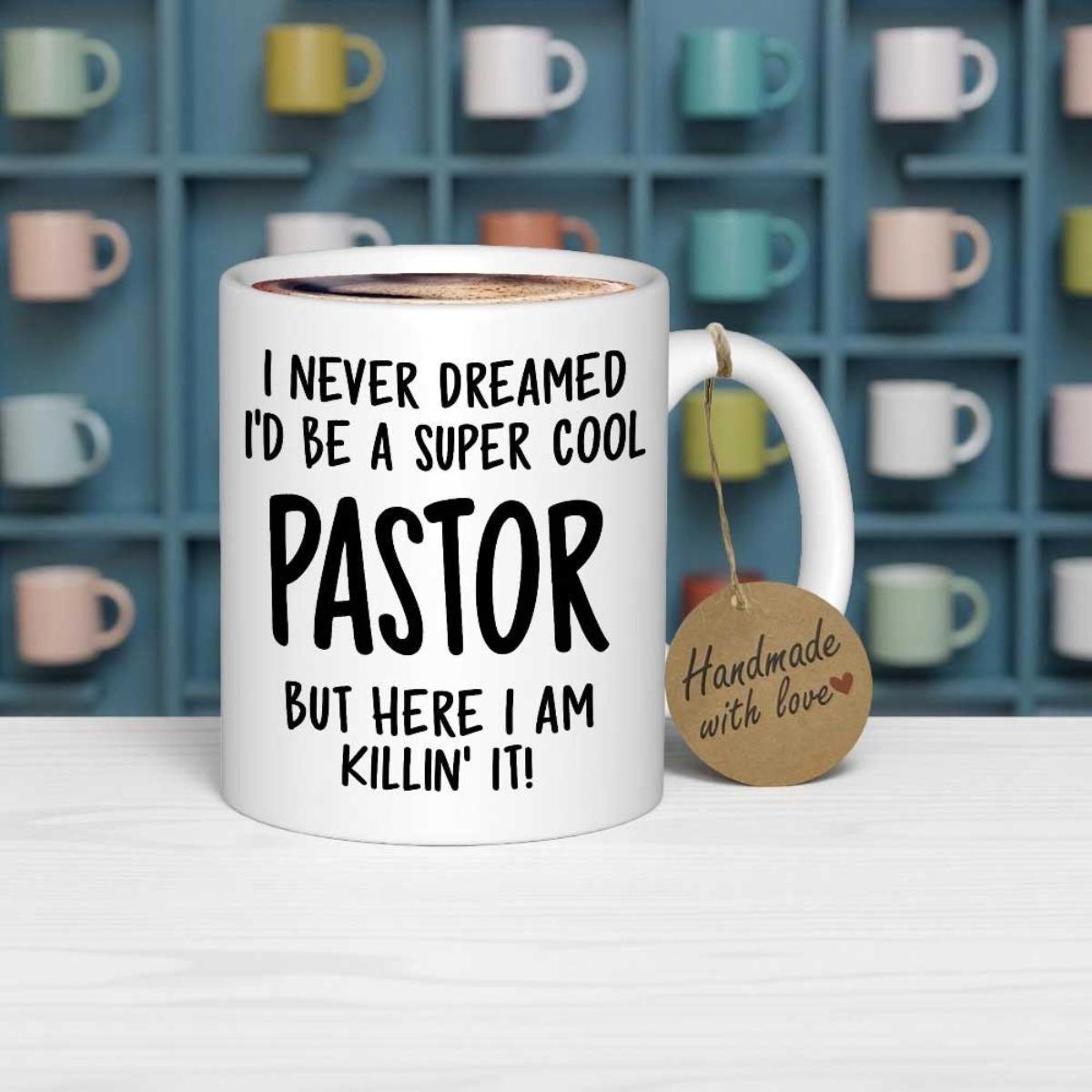 Tailorly White Ceramic 11 oz Mug - I Never Dreamed Id Be A Super Cool Pastor But Here I Am Killin It Resting On Table Near Shelf Background Mug