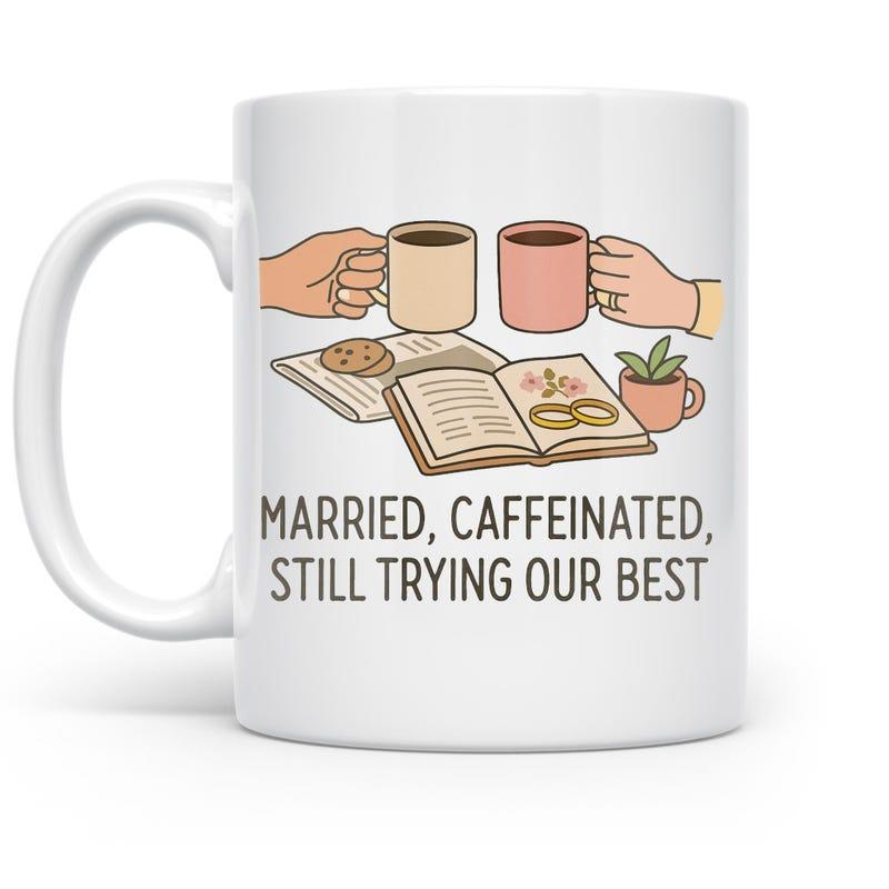 Tailorly White Ceramic 11 oz Mug - Married Caffeinated Still Trying Our Best Two Hands Holding Coffee Cups Over Open Books Beside Tiny Potted Plant Mug