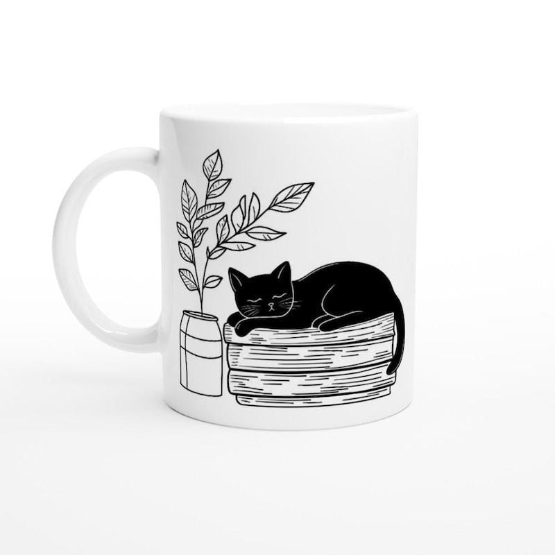 Tailorly White Ceramic 11 oz Mug - Minimalist Hand Drawn Aesthetic Resting Upon Stacked Books Beside Leafy Plant Cat