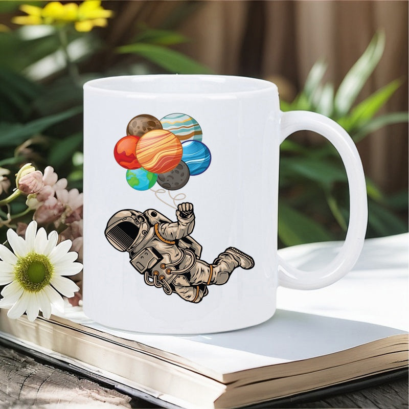 Tailorly White Ceramic 11 oz Mug - Floating In Outer Space Holding Colorful Planet Shaped Balloons Astronaut