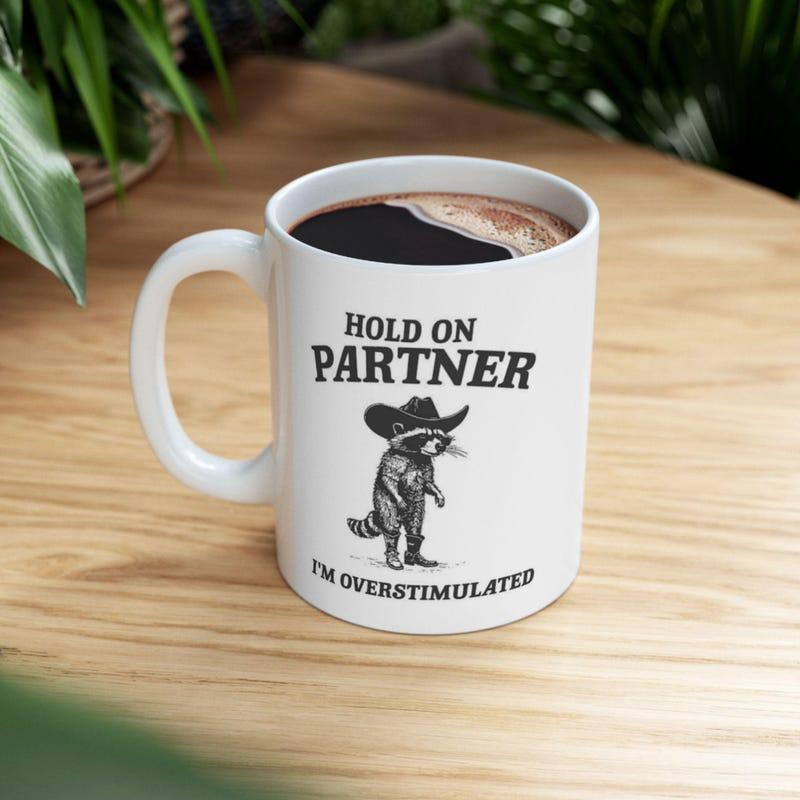 Tailorly White Ceramic 11 oz Mug - Hold On Partner Im Overstimulated Stylized Vintage Illustration Wearing Western Cowboy Hat And Boots Raccoon