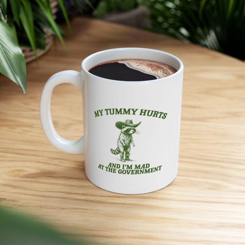 Tailorly White Ceramic 11 oz Mug - My Tummy Hurts And I'm Mad At The Government Grumpy Little Creature Wearing A Rustic Green Vintage Cowboy Hat Raccoon
