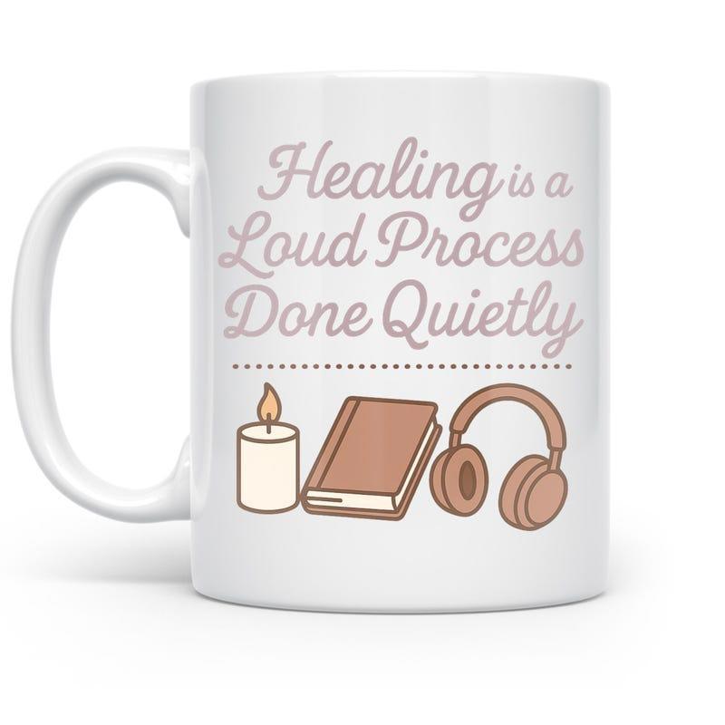 Tailorly White Ceramic 11 oz Mug - Healing Is A Loud Process Done Quietly Glowing Candle Flame Beside Resting Book And Audio Headphones