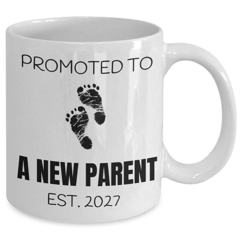 Tailorly White Ceramic 11 oz Mug - Promoted To A New Parent Est 2027 Delicate Black Infant Ink Marks Resting Against A Smooth Footprints