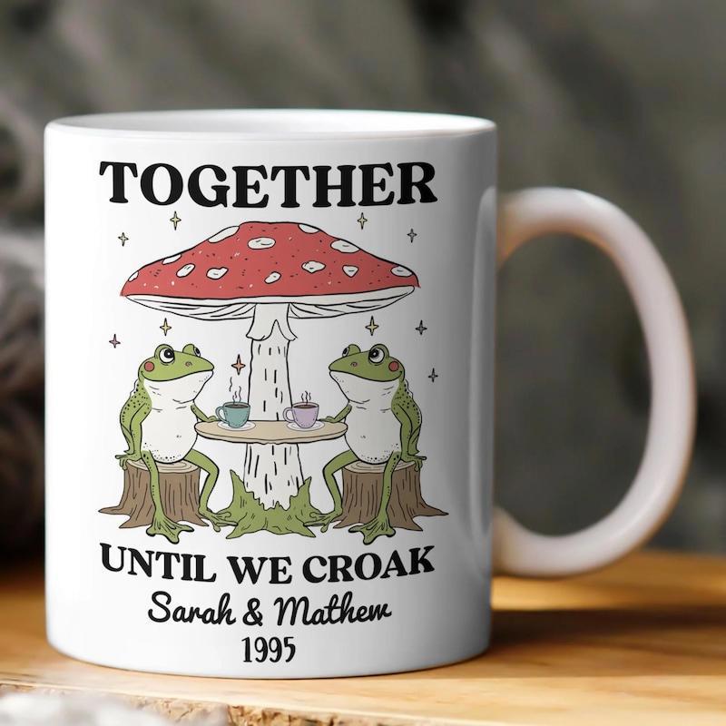 Tailorly White Ceramic 11 oz Mug - Together Until We Croak Sarah Mathew 1995 Two Green Frogs Drinking Tea Under A Large Spotted Mushroom Frog