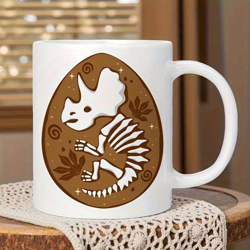 Tailorly White Ceramic 11 oz Mug - Stylized White Triceratops Skeleton Resting Within A Decorative Brown Earthy Egg Dinosaur