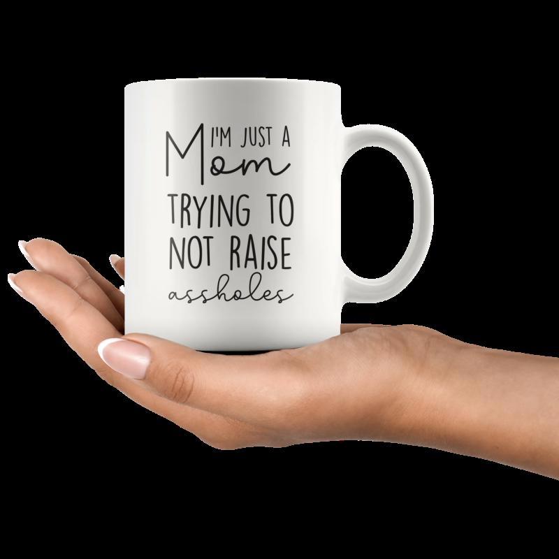 Tailorly White Ceramic 11 oz Mug - Im Just A Mom Trying To Not Raise Assholes Minimalist White Ceramic Vessel Displayed On A Gentle Human Hand Mug