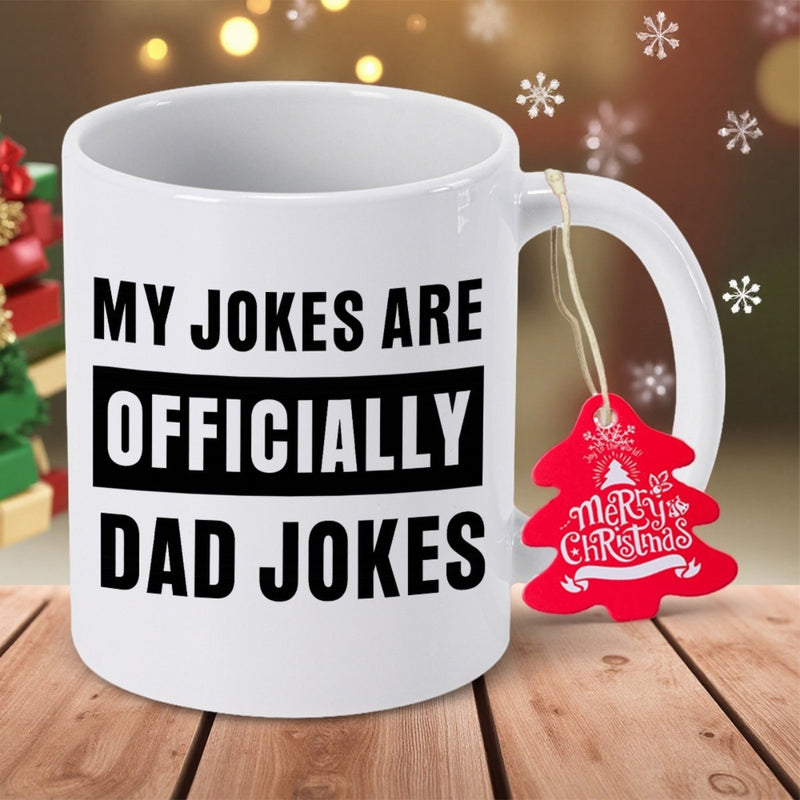 Tailorly White Ceramic 11 oz Mug - My Jokes Are Officially Dad Jokes Festive Holiday Setting Over Wooden Surface With Decorative Red Christmas Tree Tag Mug
