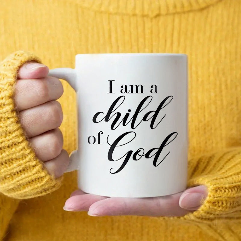 Tailorly White Ceramic 11 oz Mug - I Am A Child Of God Minimalist Ceramic Vessel Held By Hands Against A Yellow Sweater Background Mug
