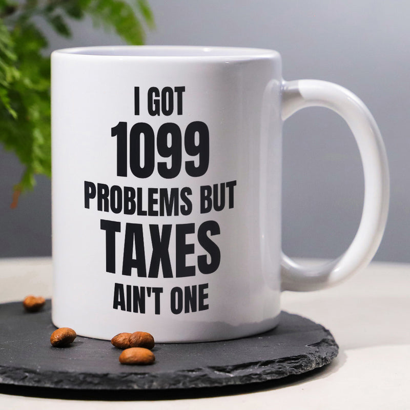 Tailorly White Ceramic 11 oz Mug - I Got 1099 Problems But Taxes Ain't One Minimalist Ceramic Vessel Featuring Bold Black Typography Resting On Dark Slate Mug